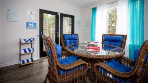 A dining area with wicker chairs and a glass table, a pool rules sign, and a shelf with towels. - Quaint home w/ Private Pool Near Lake Murray – Ideal for Families and Friends (Columbia)