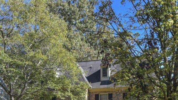 A two-story brick house with a front porch, a small garden, and a clear blue sky. - Quaint home w/ Private Pool Near Lake Murray – Ideal for Families and Friends (Columbia)