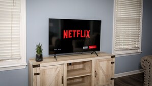 A television on a wooden cabinet with a plant on top, set against a blue wall. - Quaint home w/ Private Pool Near Lake Murray – Ideal for Families and Friends (Columbia)