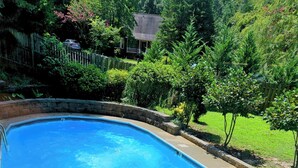 A swimming pool with a curved edge, surrounded by a concrete deck and a wooden fence. - Quaint home w/ Private Pool Near Lake Murray – Ideal for Families and Friends (Columbia)