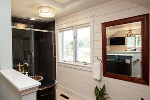 A bathroom with a glass shower enclosure, a white sink, a mirror with a wooden frame, and a window with a view of the outside. - River House in historic Rockton, IL (Rockton)