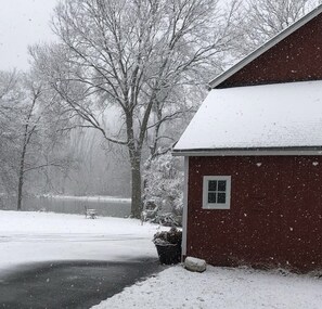 A red barn with a snow-covered roof, a bench, and a tree in the background. - River House in historic Rockton, IL (Rockton)