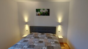Ein Schlafzimmer mit dunklem Kopfteil, einer gesteppten Bettdecke, zwei Nachttischlampen und einem Wandbild mit weißen Blüten.