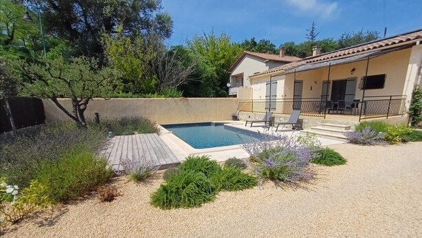Ein Poolbereich mit einer kleinen Terrasse, umgeben von Kies und Pflanzen, und ein Gebäude mit einem Ziegeldach im Hintergrund.