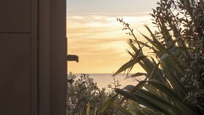 En træterrasse der fører hen til en bygning, med udsigt til solnedgangen over havet.