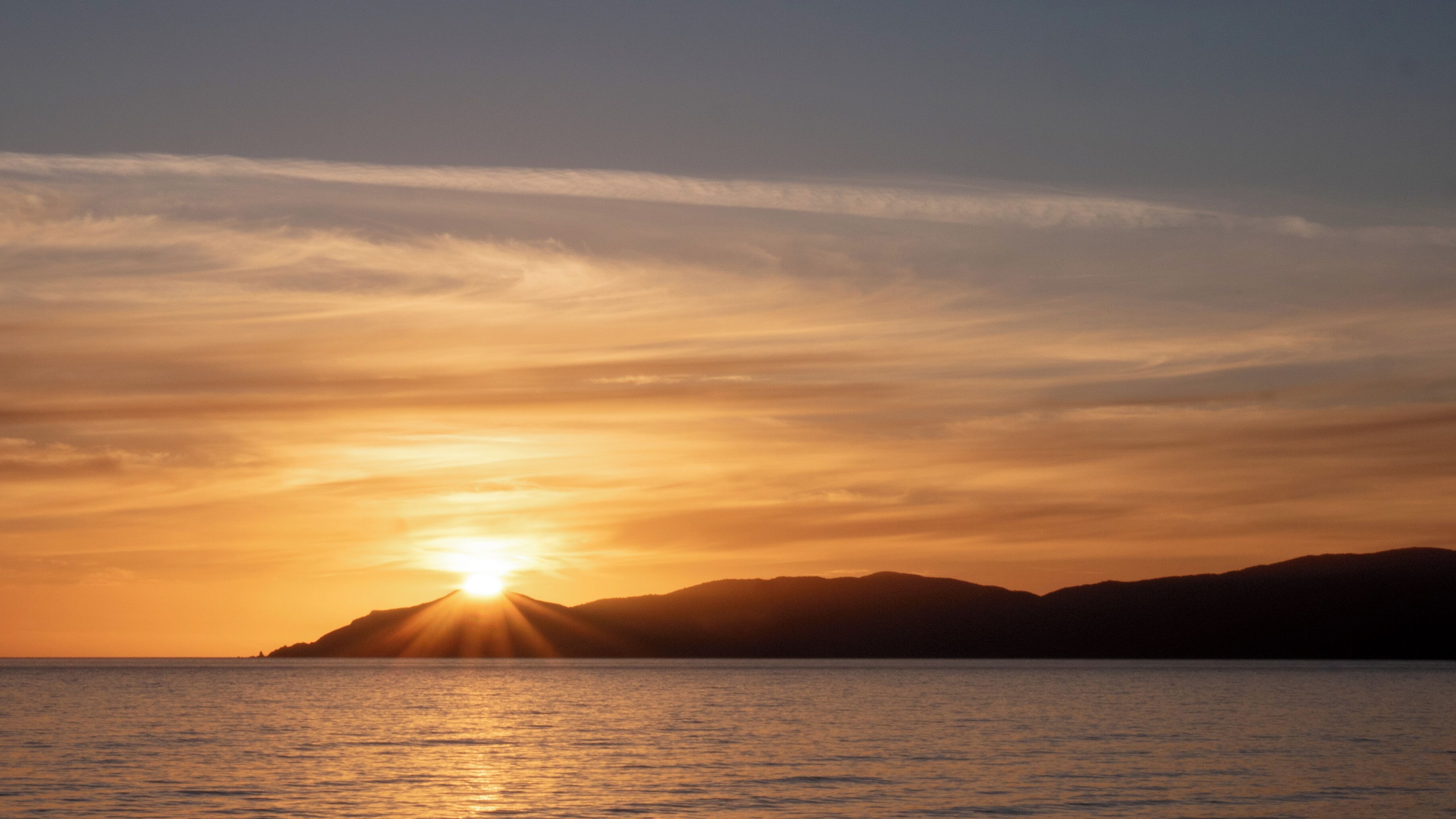 Un atardecer sobre un mar tranquilo, con siluetas de tierras lejanas delineándose en el cielo.