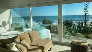 En moderne stue med en stor glasdør, der fører ud til en balkon med udsigt over havet.