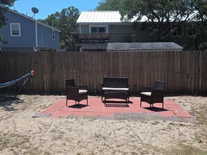 A fenced backyard with three wicker chairs on a red brick patio.