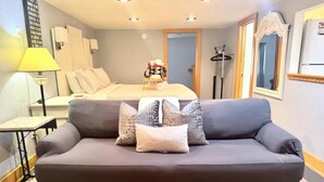 Een moderne hotelkamer met een grijze bank, een houten salontafel, een bed met een wit hoofdeinde, en een spiegel aan de muur.