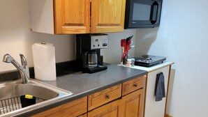 Een keuken met houten kastjes, een roestvrijstalen spoelbak, een koffiezetapparaat, een magnetron en een klein aanrecht met een messenblok.