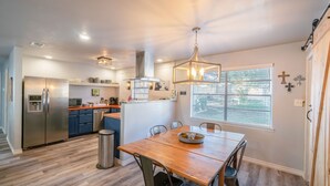 A modern kitchen with a wooden dining table, stainless steel appliances, and a large window. - Trendy Pet-friendly House w/ Patio near Lake LBJ (Kingsland)
