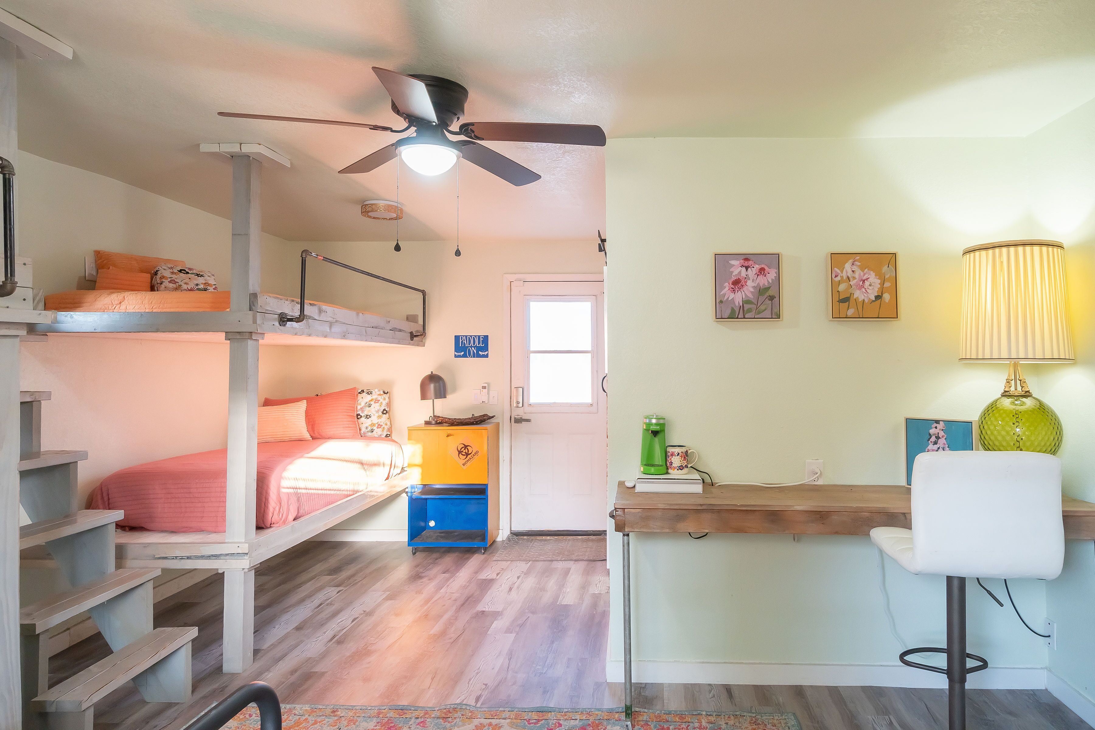 A compact room with bunk beds, a desk, a chair, a ceiling fan, and a lamp.