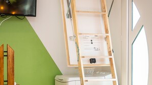 Huoneessa on seinää vasten nojaava puinen tikapuu, seinälle asennettu televisio, valkoinen kodinkone ja vihreä seinä.