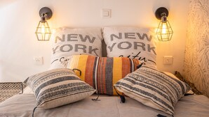 Sängyssä on kuviollisia tyynyjä ja kaksi seinälle asennettua valaisinta, joissa lukee teksti ”NEW YORK”.