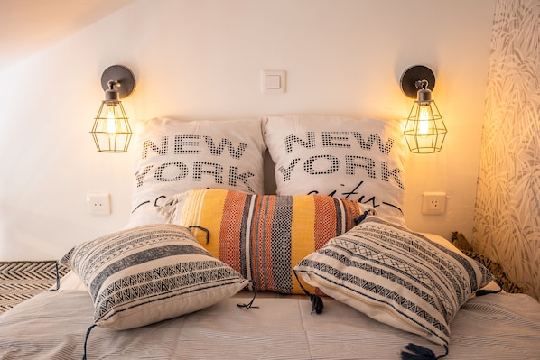 A bed with patterned pillows and two wall-mounted light fixtures with the text "NEW YORK" on them.