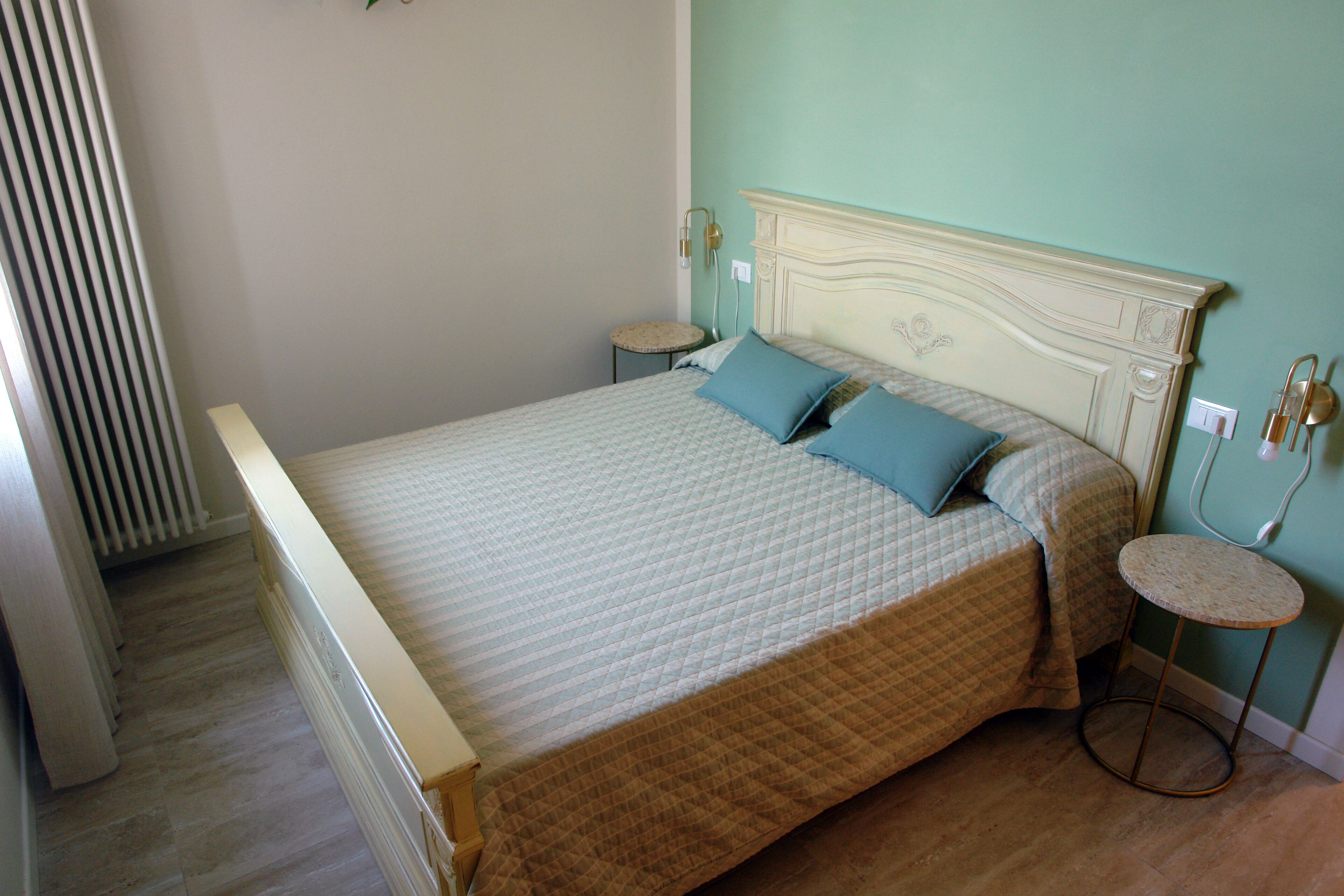 A bedroom with a bed, two bedside tables, a round stool, and a radiator.