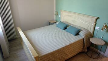 A bedroom with a bed, two bedside tables, a round stool, and a radiator.