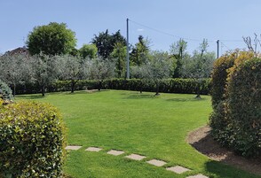 Un prato curato con pietre di passaggio, circondato da siepi e alberi ben potati.