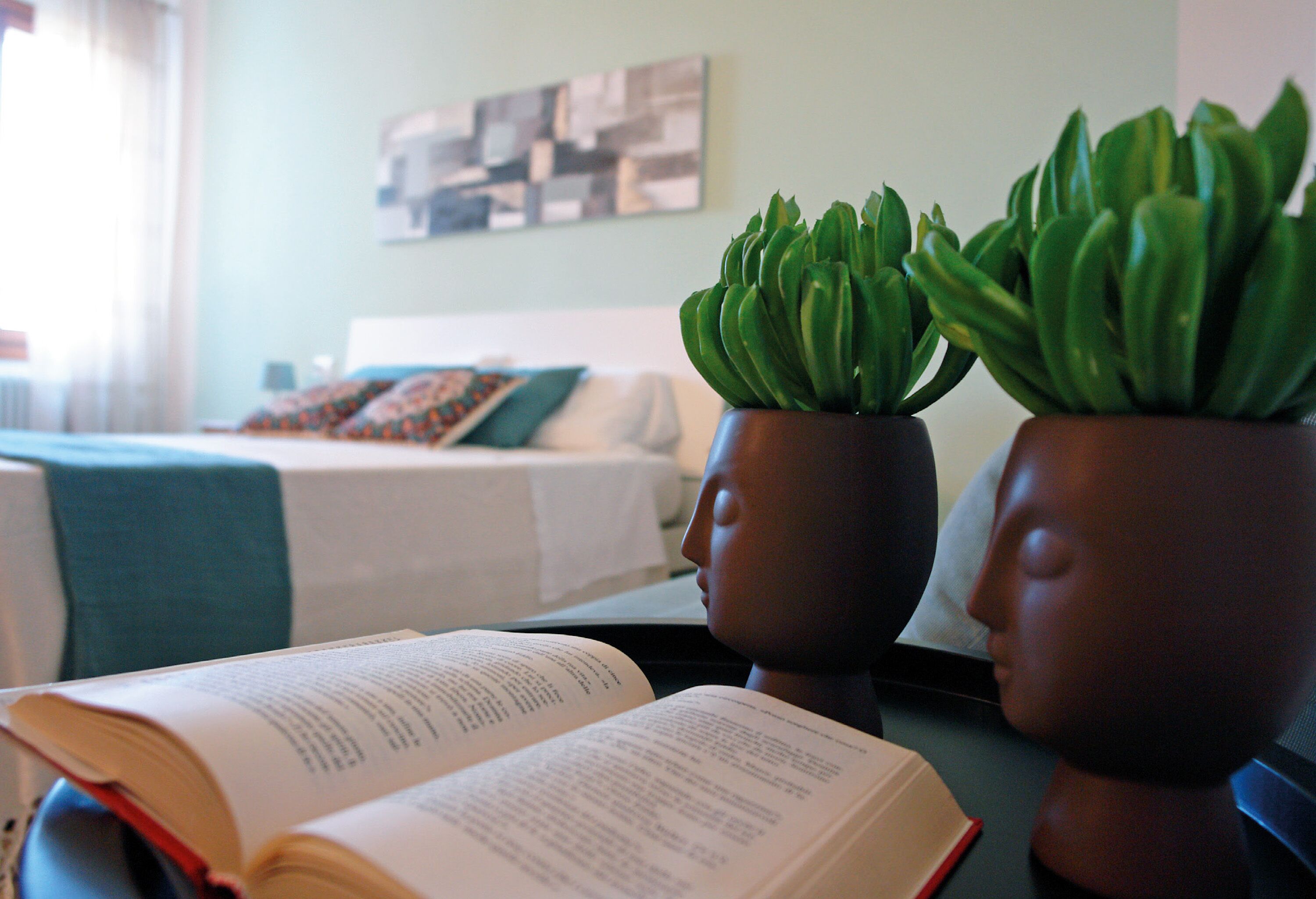 A room with a bed, a book, and two potted plants on a table.