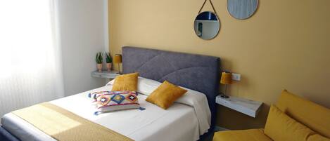 A neatly arranged bedroom with a bed, bedside tables, a mirror, and a sofa.