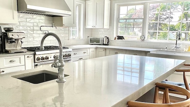 A modern kitchen with white cabinetry, a large island with bar stools, a stove, and a window with a view of trees. - Charming Summer House (newly remodeled).  4 min from the beach (FAIRFIELD)