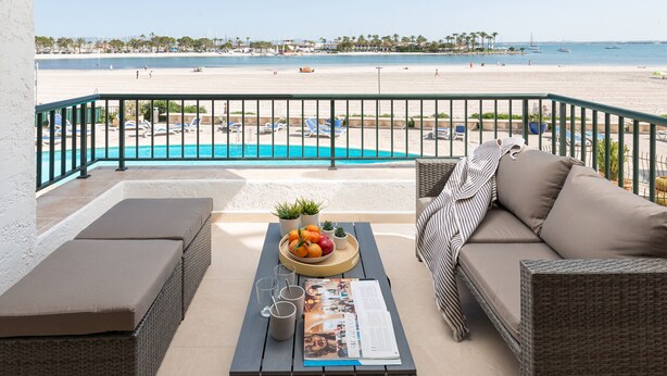 A balcony with wicker furniture, a pool, and a view of the beach. - BEACHSIDE CARABELA APARTAMENTOS (Alcúdia)