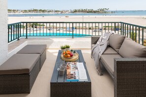 A balcony with wicker furniture, a pool, and a view of the beach. - BEACHSIDE CARABELA APARTAMENTOS (Alcúdia)
