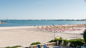 A beach with sun loungers and umbrellas, a clear sky, and boats in the water. - BEACHSIDE CARABELA APARTAMENTOS (Alcúdia)