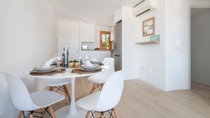 A modern kitchen with white cabinetry, a dining table with white chairs, and a small island with a sink. - BEACHSIDE CARABELA APARTAMENTOS (Alcúdia)