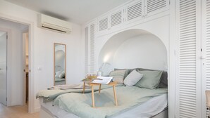 A bedroom with a bed, a bedside table with a lamp, a mirror, and a wardrobe with louvered doors. - BEACHSIDE CARABELA APARTAMENTOS (Alcúdia)