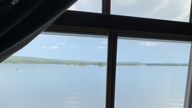 A window with a view of a calm body of water and a distant shoreline. - Railway camp on Moosehead Lake (greenville)