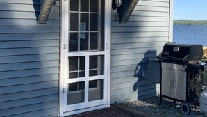 A house with a front porch, a sliding glass door, a grill, and a view of a lake. - Railway camp on Moosehead Lake (greenville)