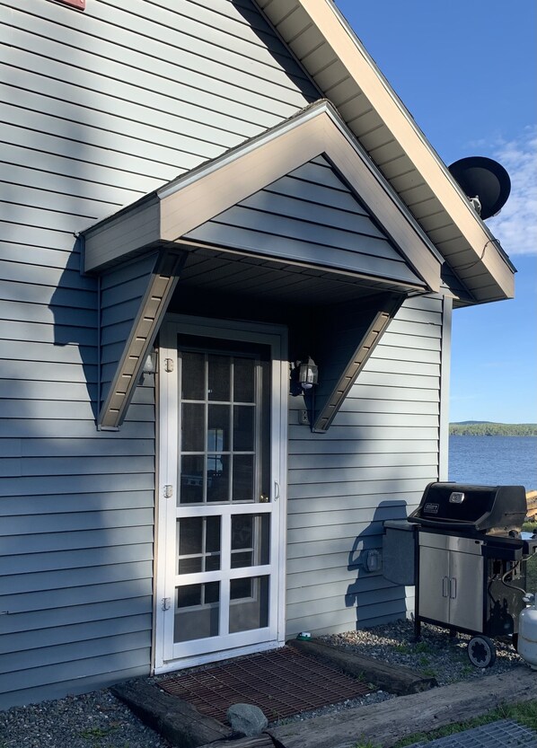 A house with a front porch, a sliding glass door, a grill, and a view of a lake.