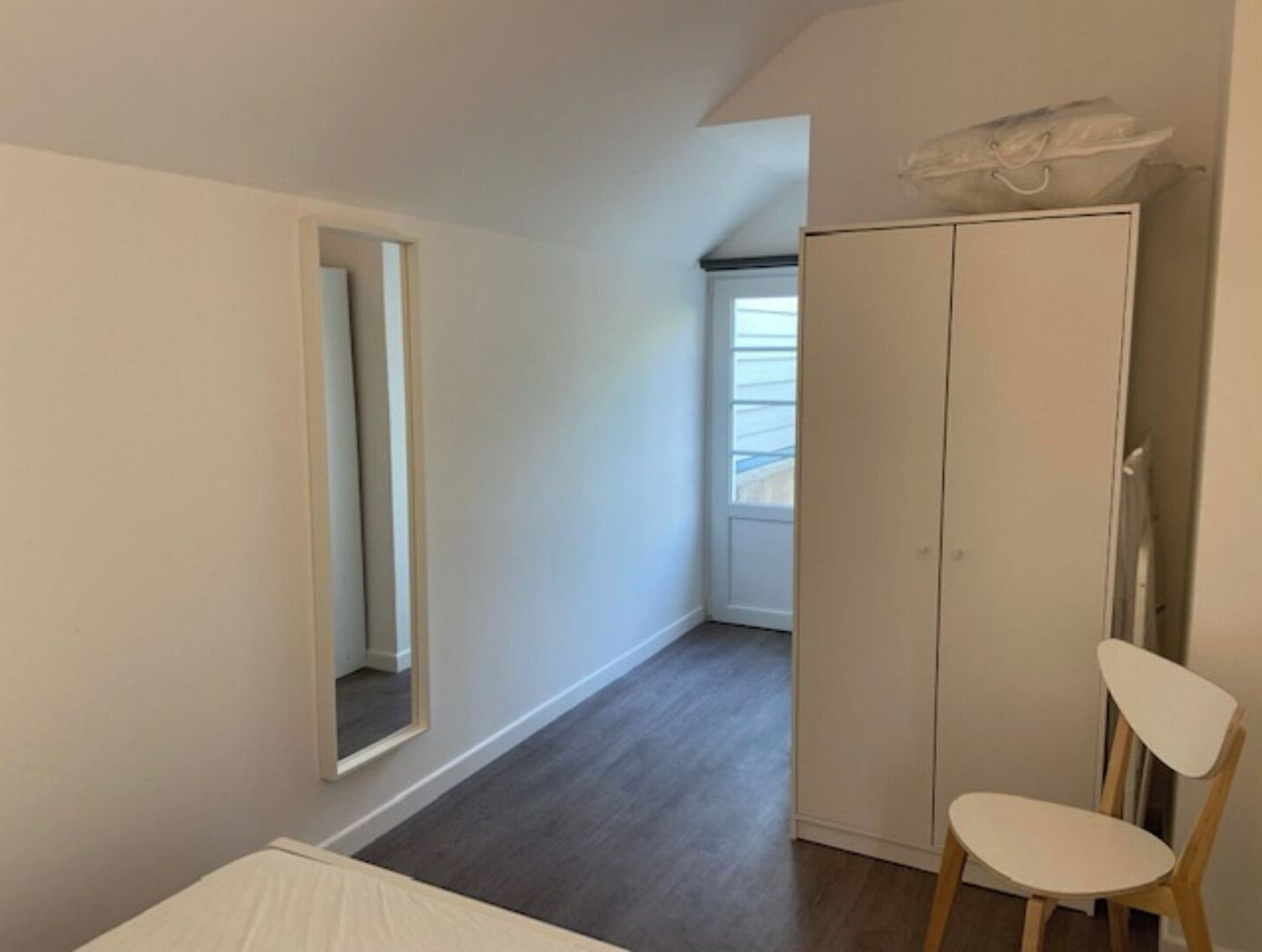Una camera da letto con un letto, un armadio, una sedia e uno specchio.