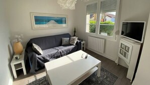 A living room with a sofa, a coffee table, a TV, and a window with blinds. - Villa POPEE for 8 people (Cucq)