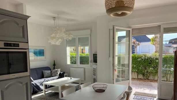 A modern kitchen with a dining area, a sofa, and a view of the garden through the open door. - Villa POPEE for 8 people (Cucq)