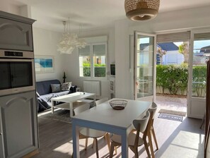 Une cuisine moderne avec un coin repas, un canapé et une vue sur le jardin, accessible par une porte ouverte.