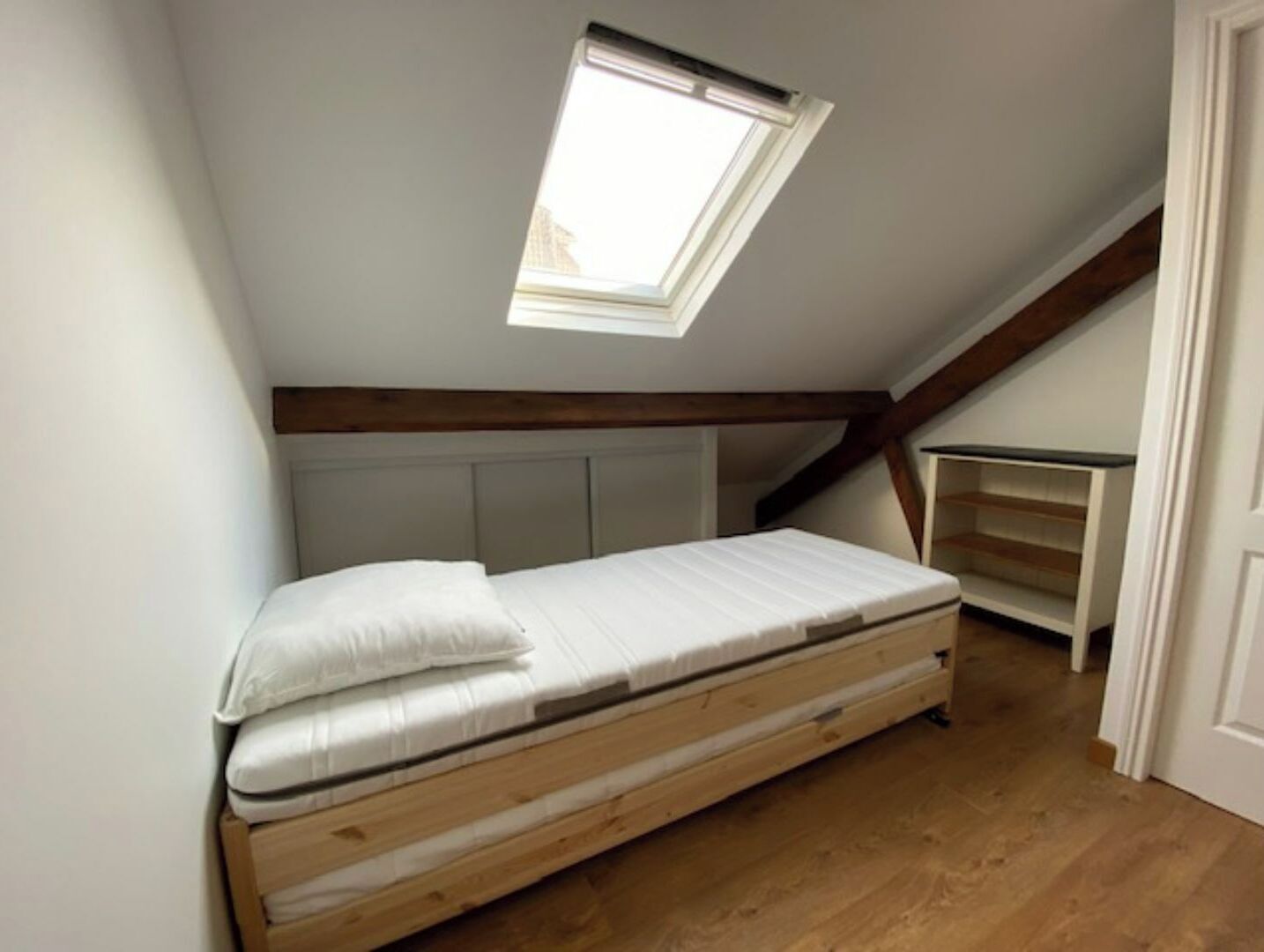 Dormitorio con techo inclinado, tragaluz, suelo de madera y cama sencilla.
