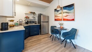 A modern kitchen with blue cabinets, a stainless steel refrigerator, and a dining area with two blue chairs and a small table. - Close to downtown, with a llama, alpaca, and others animlas on the property (Thousand Oaks)