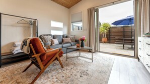 A spacious living room with a wooden ceiling, a grey sofa, a wooden chair, a coffee table, and a view of an outdoor patio with a table and umbrella. - Close to downtown, with a llama, alpaca, and others animlas on the property (Thousand Oaks)
