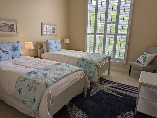 A bedroom with two beds, a window with blinds, a lamp, and a chair.
