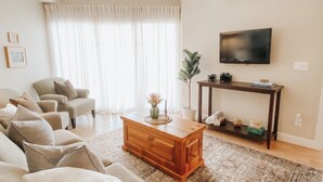 A living room with a sofa, a coffee table, a TV, and a plant. - Okanagan four seasons paradise with shared pool and hot tub (Westbank)
