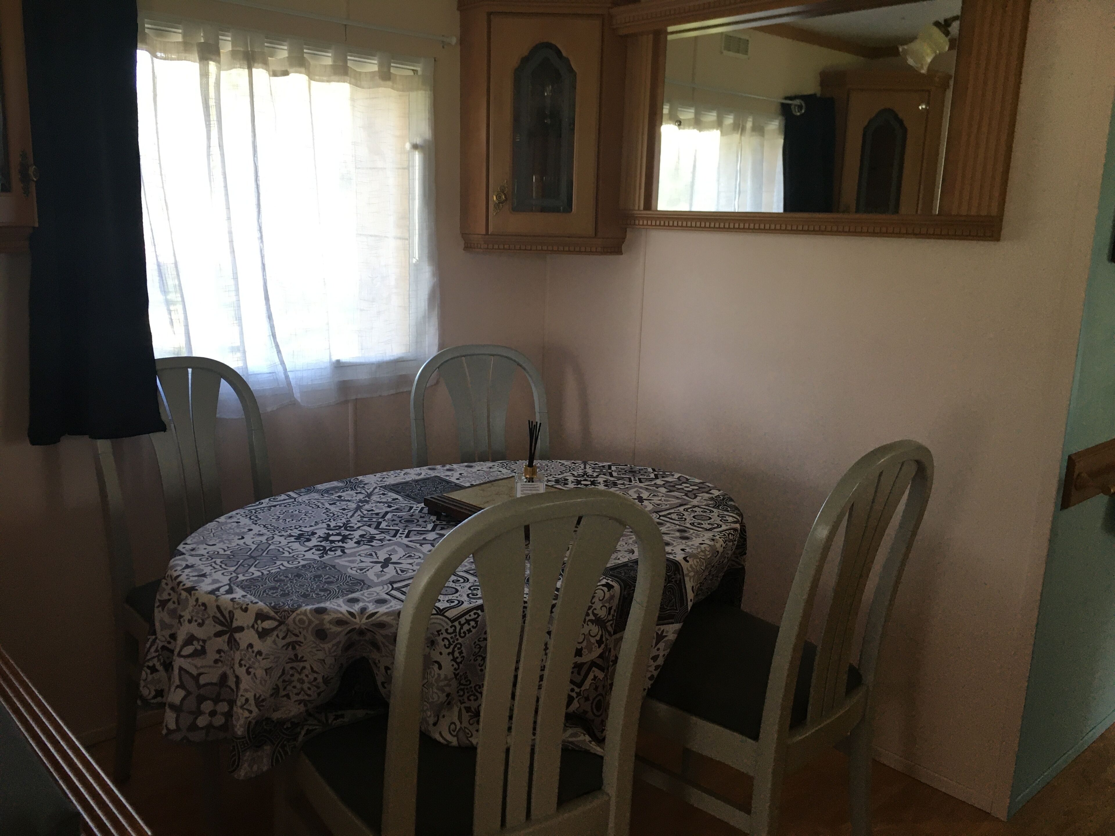 Un comedor con una mesa redonda cubierta por un mantel estampado, rodeado de cuatro sillas blancas.