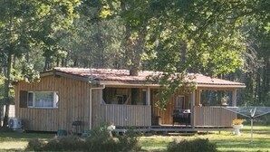 Una cabaña de madera con porche y una pequeña terraza, rodeada de árboles.