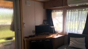 Interior compacto de una autocaravana con kitchenette, un pequeño escritorio con computadora y una zona de estar con cojín.
