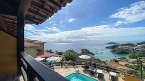 Ein Poolbereich mit Liegestühlen und Sonnenschirmen mit Blick auf die Küste, wo Boote fahren und eine Insel in der Ferne liegt.
