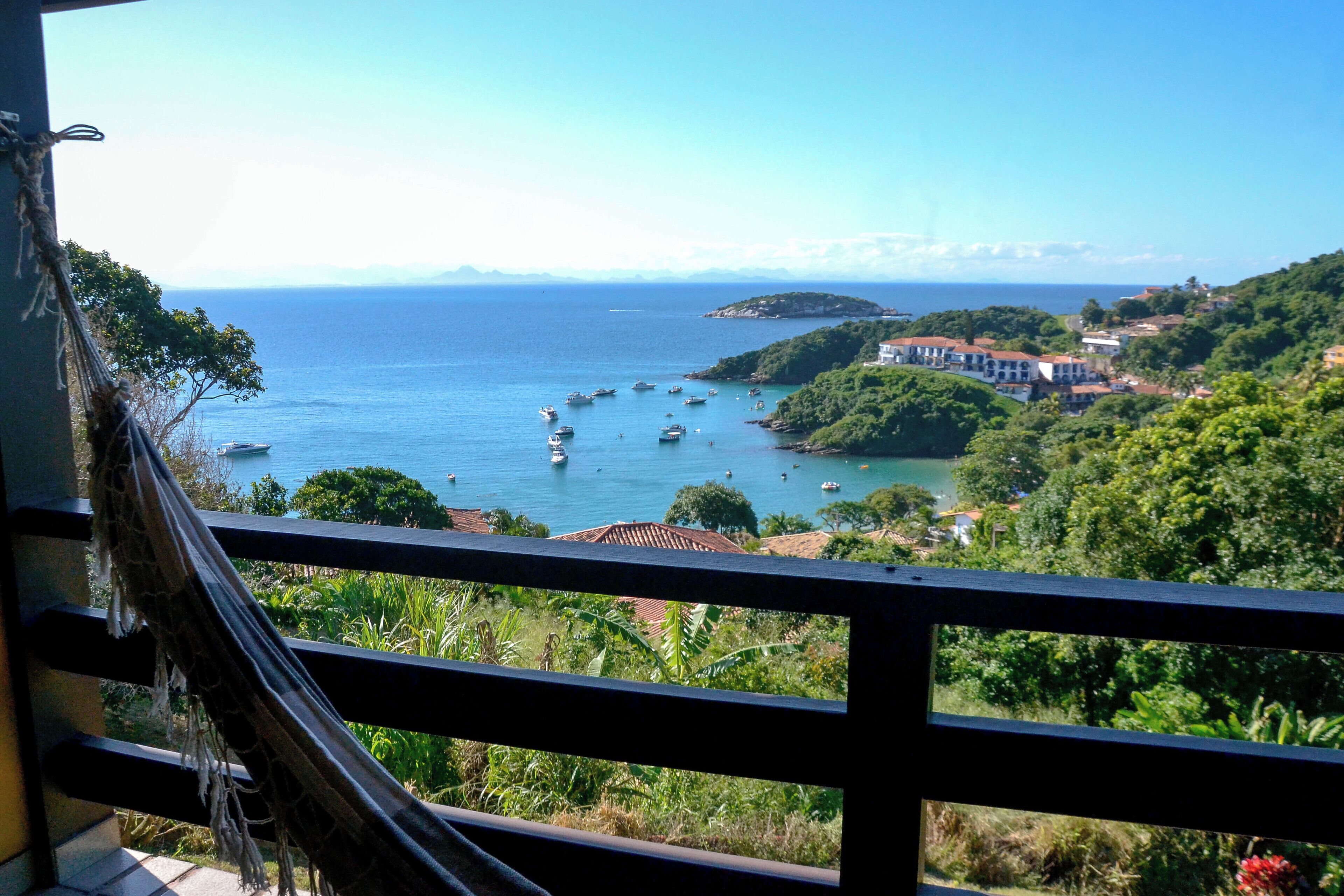 A coastal view from a balcony with a railing, boats in the water, and buildings on the hillside.