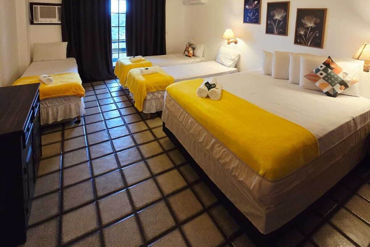 A hotel room with two beds, a desk, a window with curtains, and a ceiling with a striped pattern.