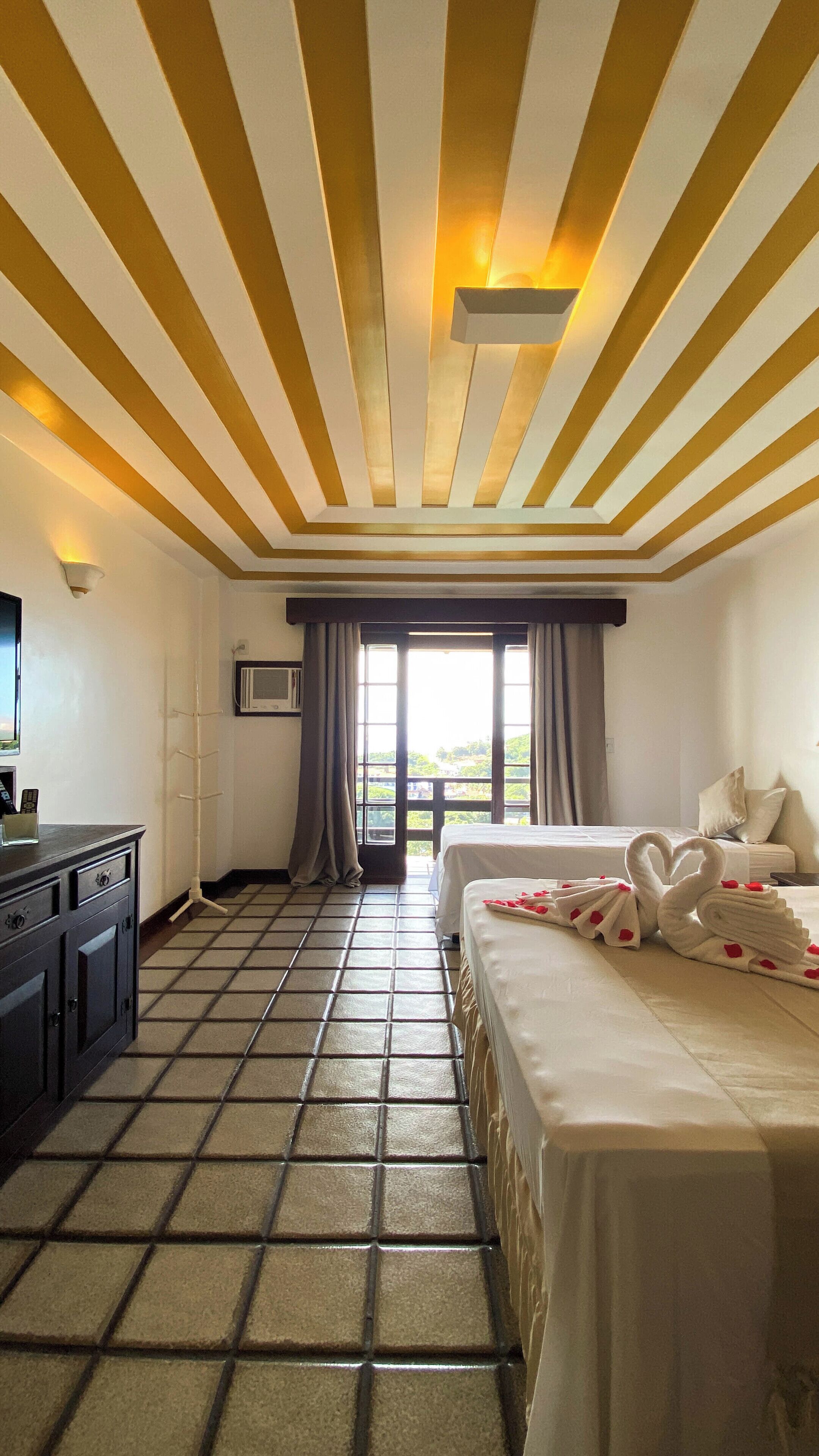 Una habitación de hotel con cama, escritorio, televisor y ventana con cortinas.