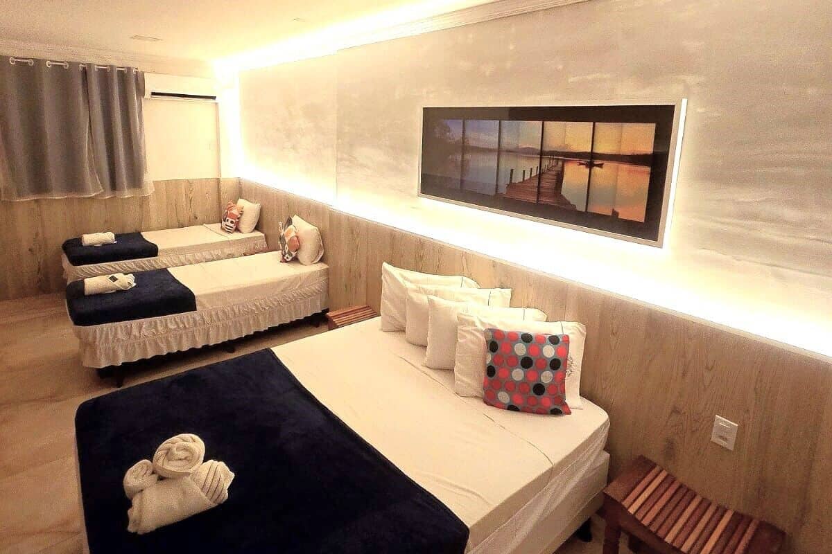 A modern bedroom with two beds, a bench, and a wall-mounted TV.